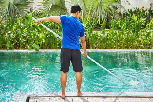 Young man cleans pool in his back yard